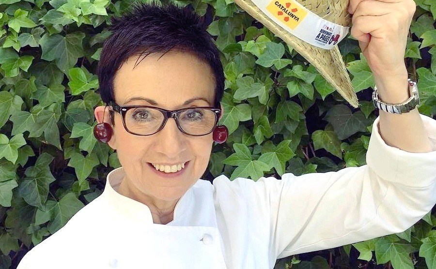 Carme Ruscalleda (7 Michelin Stars) is holding a straw hat while there are sweet cherries on her ears