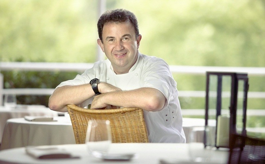 Martin Berasategui (8 Michelin Stars) is sitting on the chair in the restaurant and smiling 