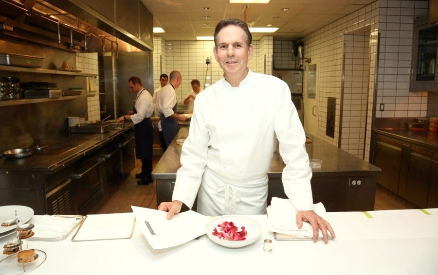 Thomas Keller (7 Michelin Stars) is in the kitchen and holding a piece of paper while other cooks are preparing dishes